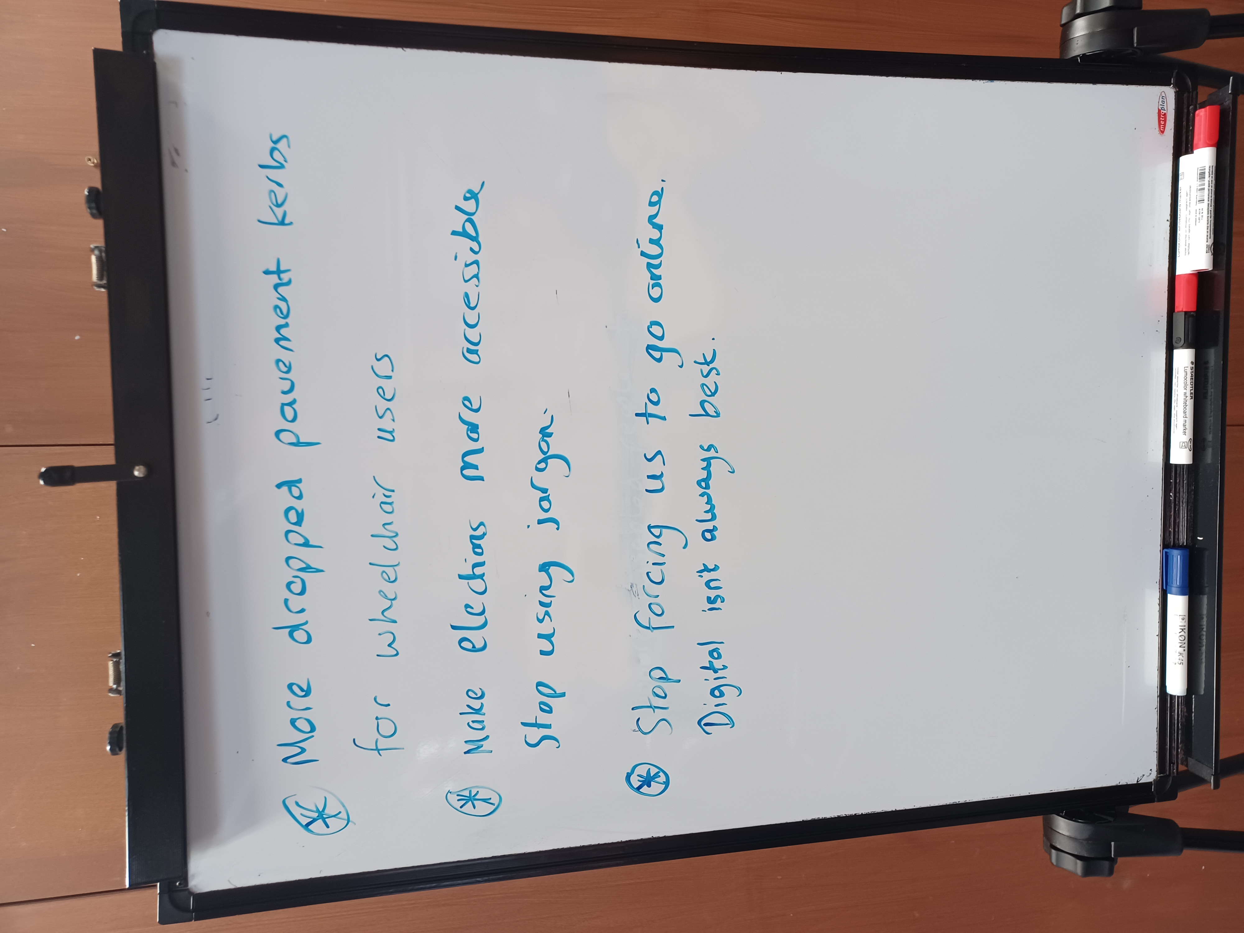 white board which says 'more dropped pavement kerbs for wheelchairs users, make elections more accessible, stop using jargon, stop forcing us to go online. Digital isn't always best'