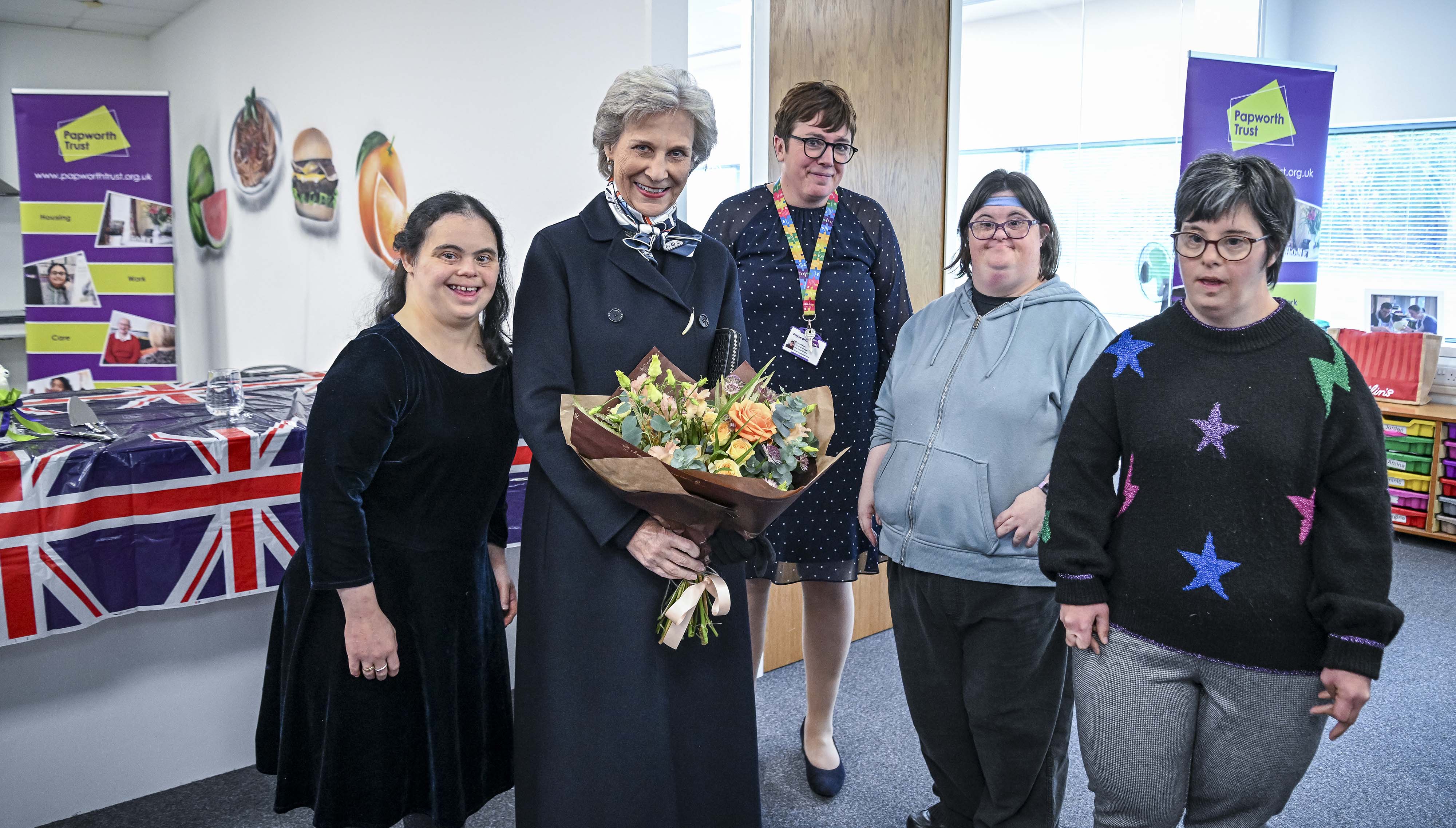 Her Royal Highness The Duchess of Gloucester holding a bouquet of flowers surround by 4 people